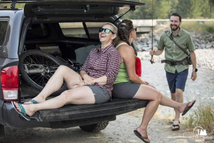 Lorenzo walks to two women sitting on a tailgate after fishing, everyone laughing. Summer in Bozeman, Montana.