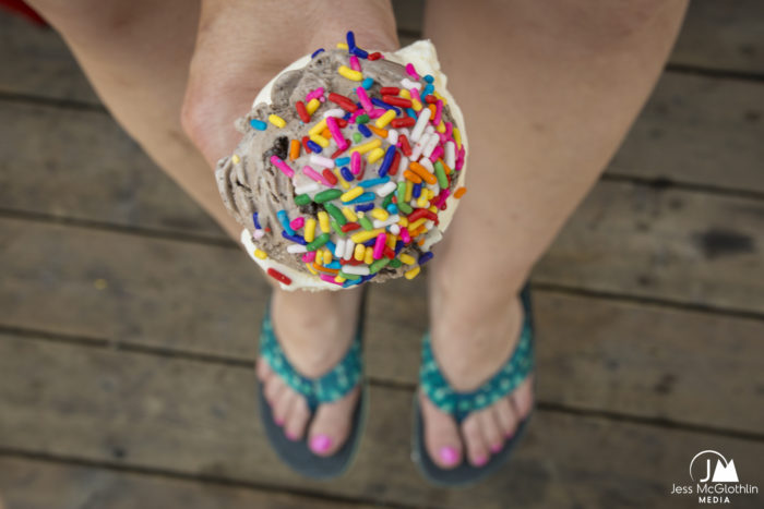 Woman holds ice cream cone with sprinkles while wearing flip-flops during summer in Montana.